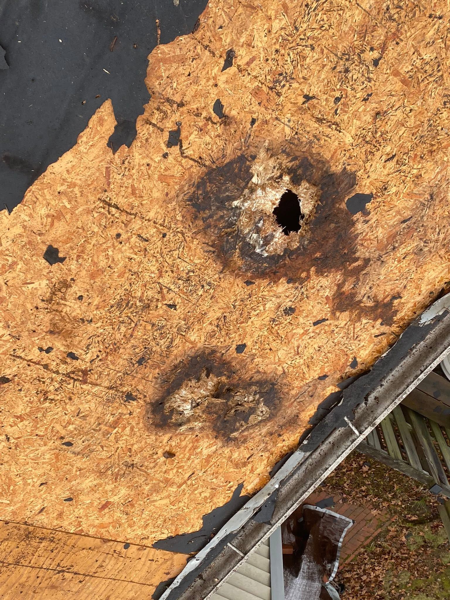 Rusty, damaged metal roof with a hole and dark burnt patches, viewed close up.