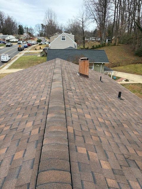 Rooftop view of brown shingle roof with chimney, neighboring houses, and a tree-lined suburban street