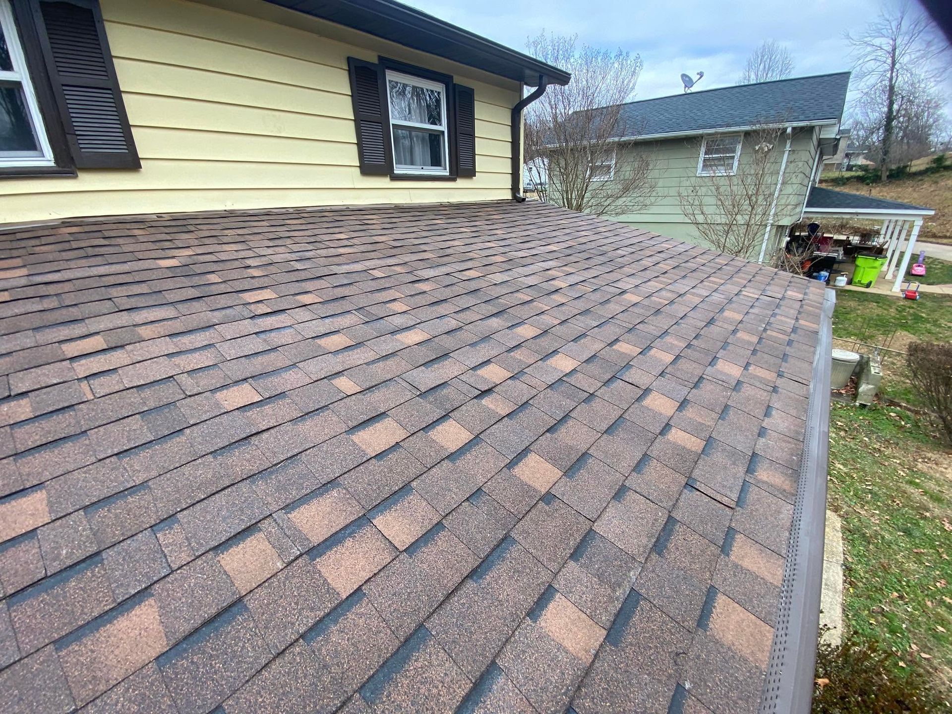Brown shingle roof on a beige house with black shutters, viewed from above.