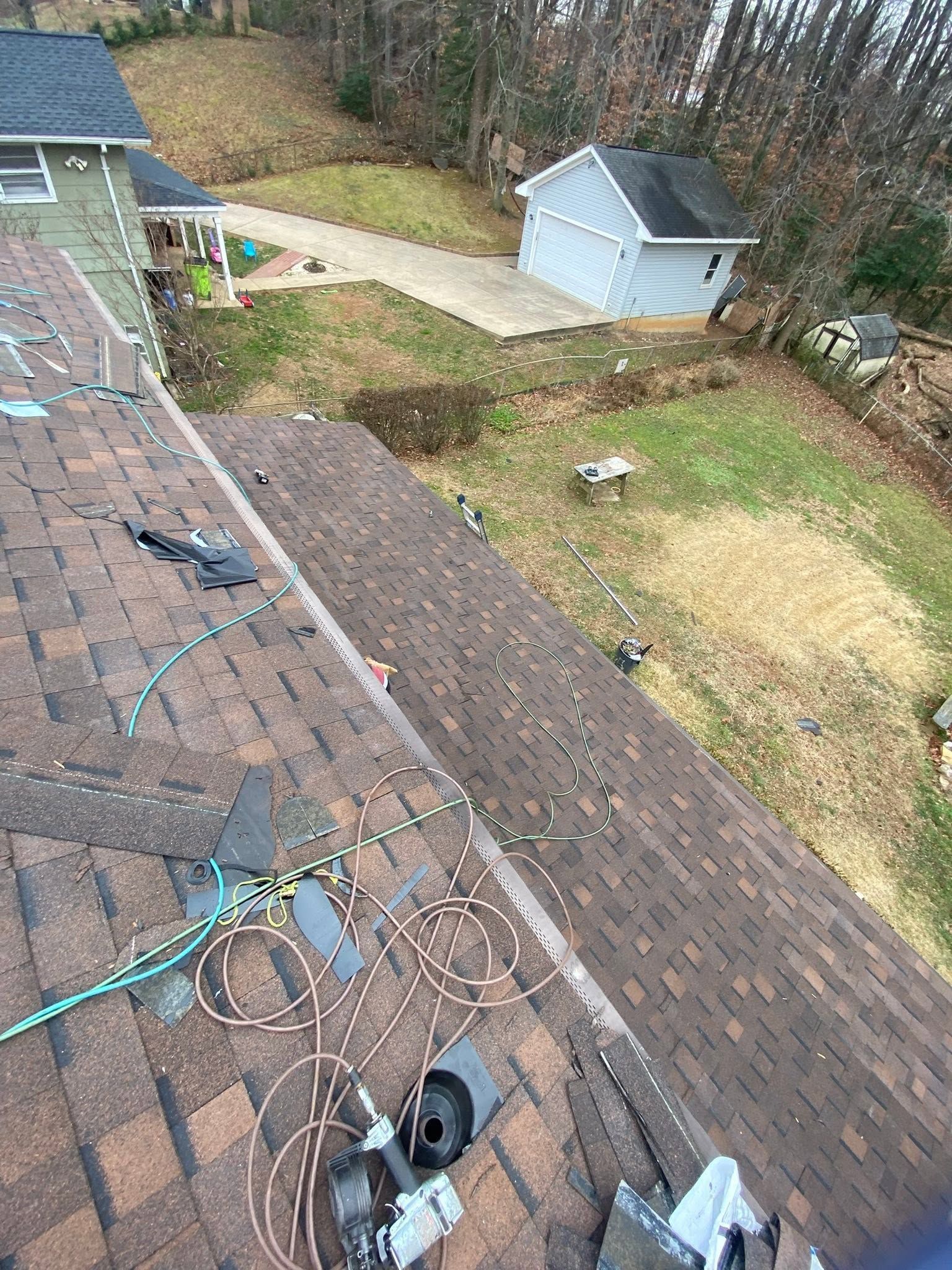 View from a roof with tools and extension cords, overlooking a backyard with sheds and a patio.