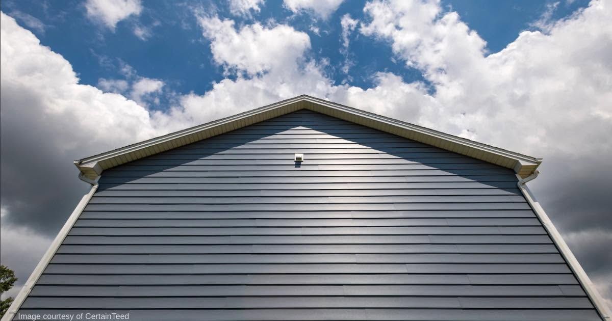 Gray siding on a house gable against a blue sky with clouds