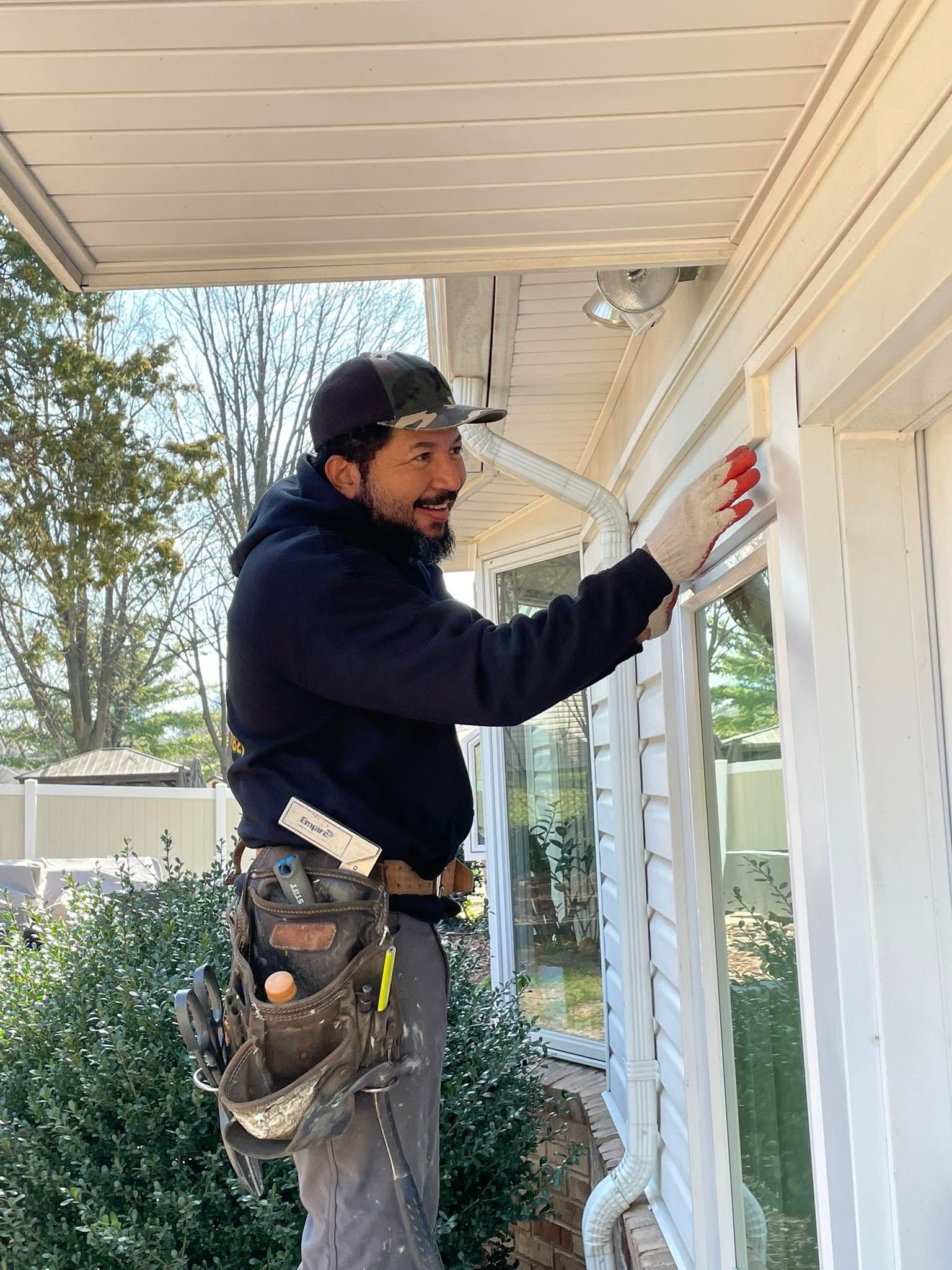 Painter on ladder painting white house trim under a porch roof