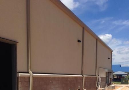 Beige industrial building wall beside a driveway under a blue sky with clouds