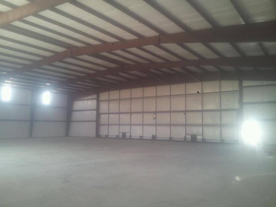 Empty industrial warehouse with steel beams, concrete floor, and bright lights near the walls