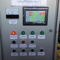 Industrial control panel with screen, gauges, and colored buttons on a gray cabinet