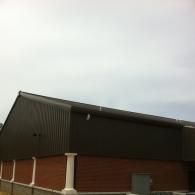 Exterior of a brick building with a dark sloped metal roof under a cloudy sky