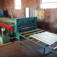 Industrial machine feeding white panels in a brick-walled workshop