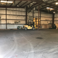 Empty warehouse interior with a yellow forklift parked near the back wall.