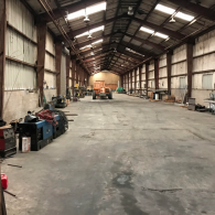 Empty industrial warehouse with a high metal roof and concrete floor, equipment along the walls