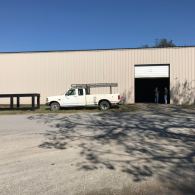 White utility truck parked beside a beige warehouse with an open garage door on a sunny day