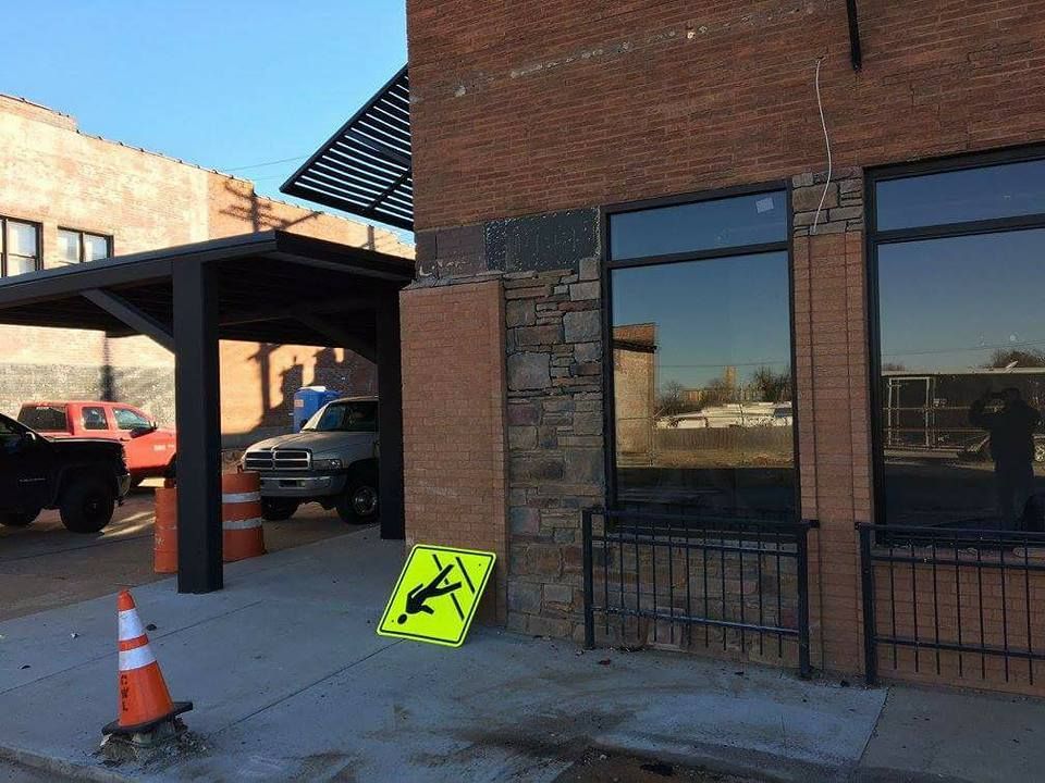 Yellow caution sign leaning against brick building beside sidewalk and covered parking area