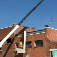 Crane lowering a worker over brick buildings under a blue sky