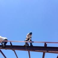 Person sitting on a steel beam high above ground against a clear blue sky
