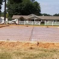 Outdoor patio under construction with fresh concrete, white fence, and a house in the background