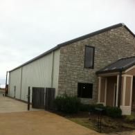 Industrial building with stone front, white side panels, and a small covered entrance