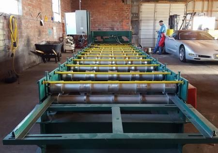 Large metal conveyor frame in a workshop with tools, a car, and two workers in the background