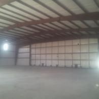 Empty industrial warehouse with concrete floor, metal beams, and a large garage door.