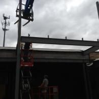 Workers on a lift installing steel beams at a construction site under a cloudy sky