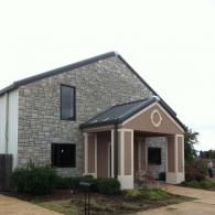Modern stone church building with a small covered entrance and a circular window above the doorway