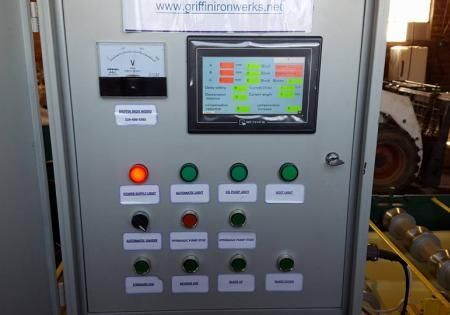 Industrial control panel with touchscreen, gauge, and illuminated buttons in a machinery room
