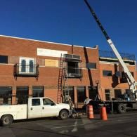 Construction workers on a lift outside a brick building, with a white pickup truck and crane nearby.