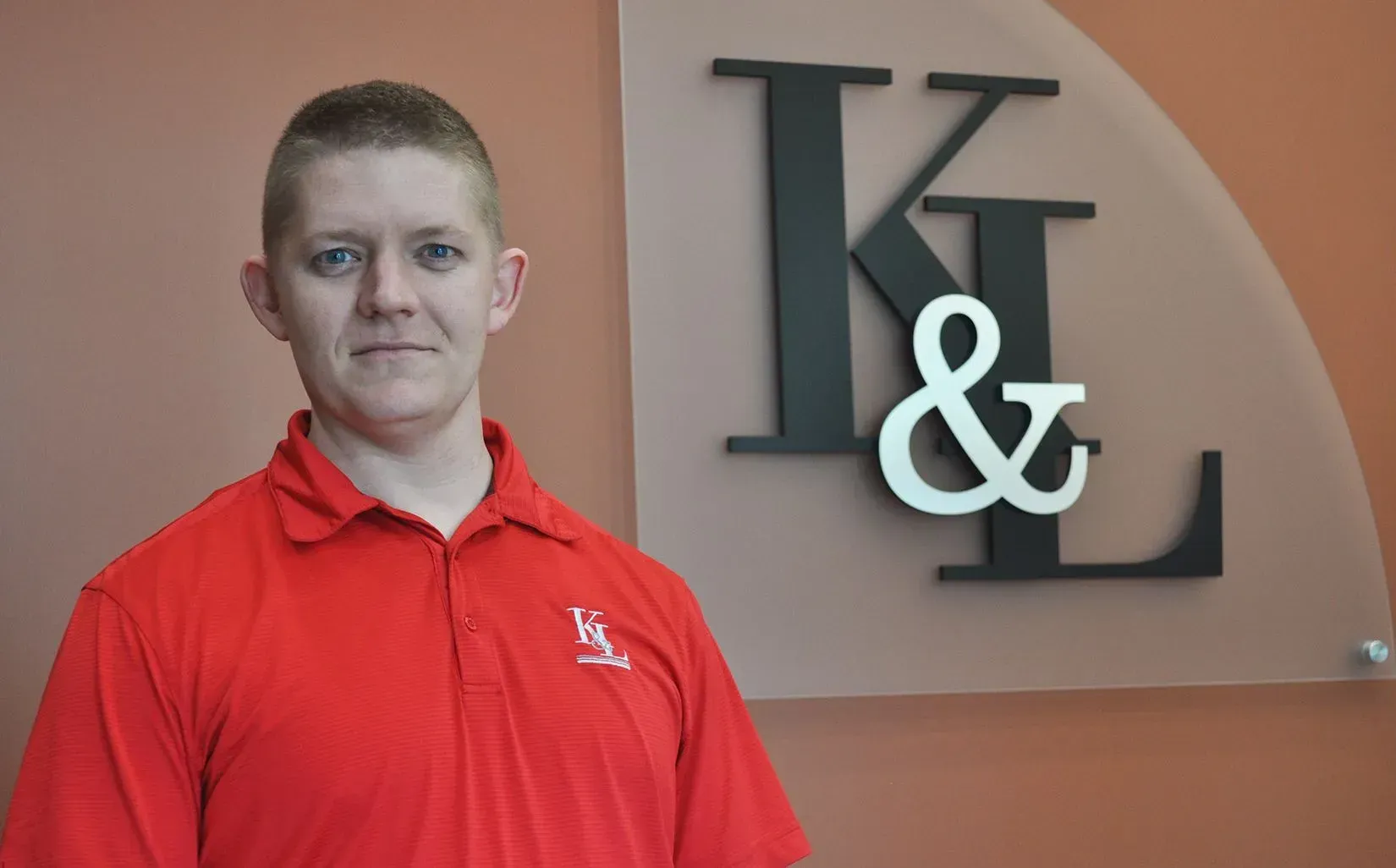 Man in red polo shirt stands in front of a wall with