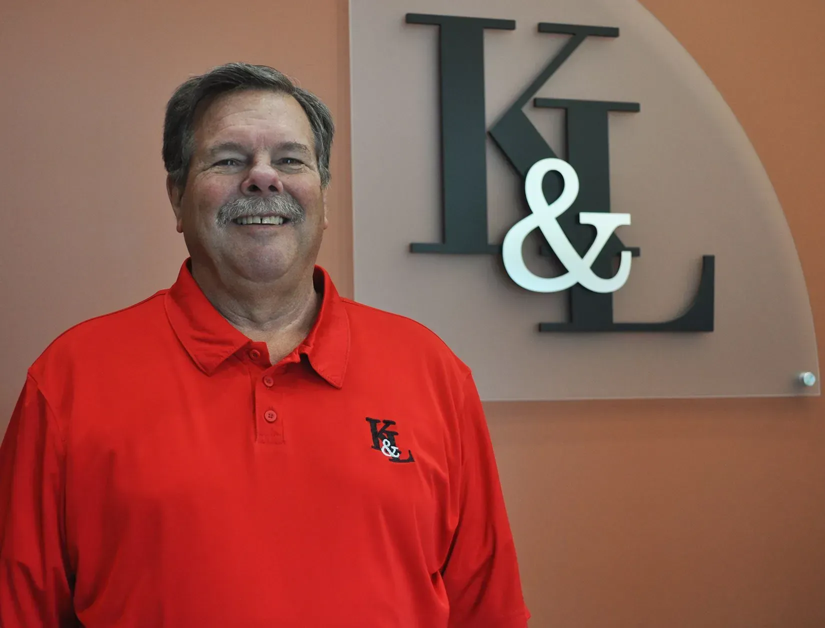 Man in red polo shirt smiles in front of a wall with