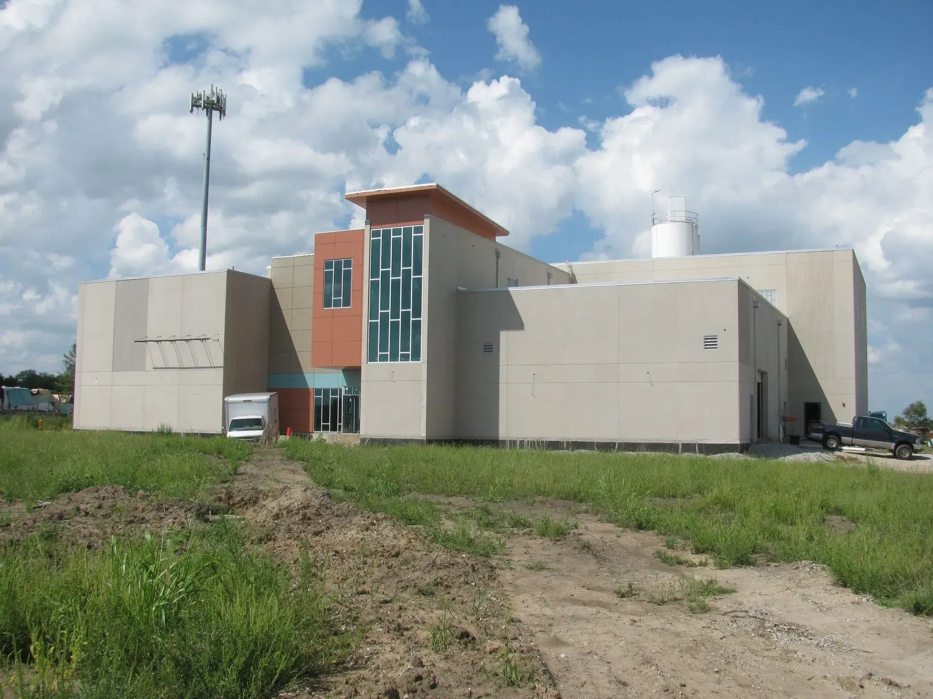 Church building with brick exterior, green roof, steeple with cross, and front entrance, under blue sky.