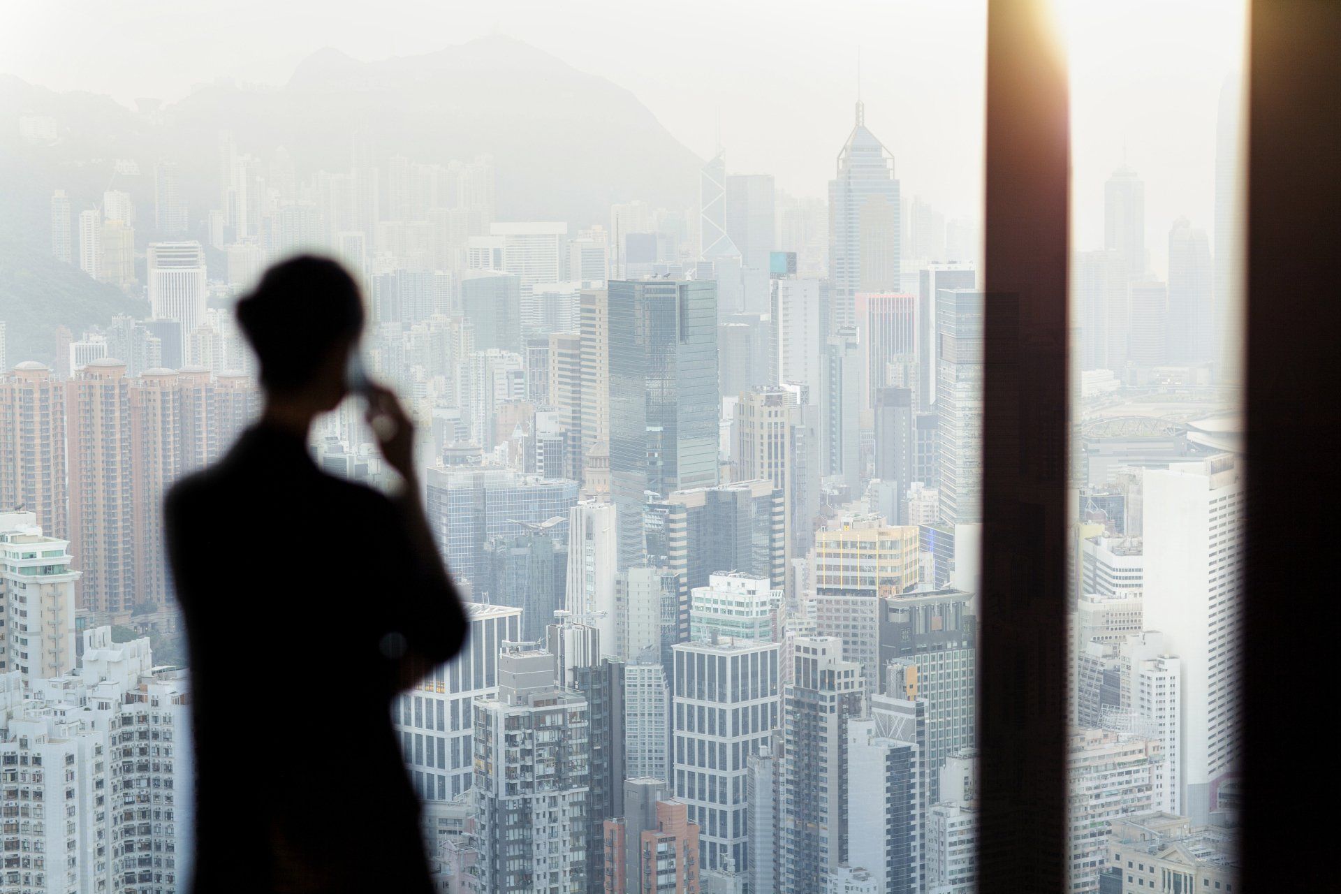 Lady on phone looking out into city scape, must be in high rise