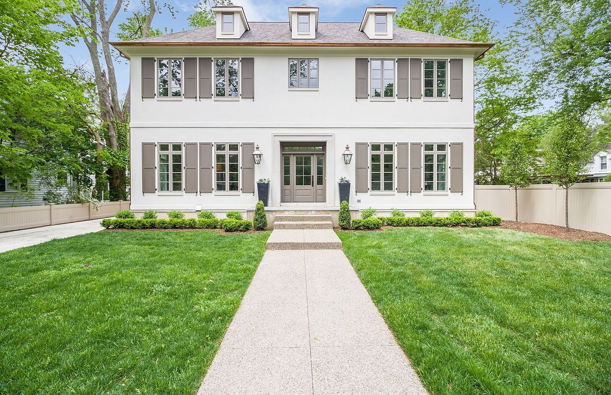 A large white house with a lush green lawn and a walkway leading to it.