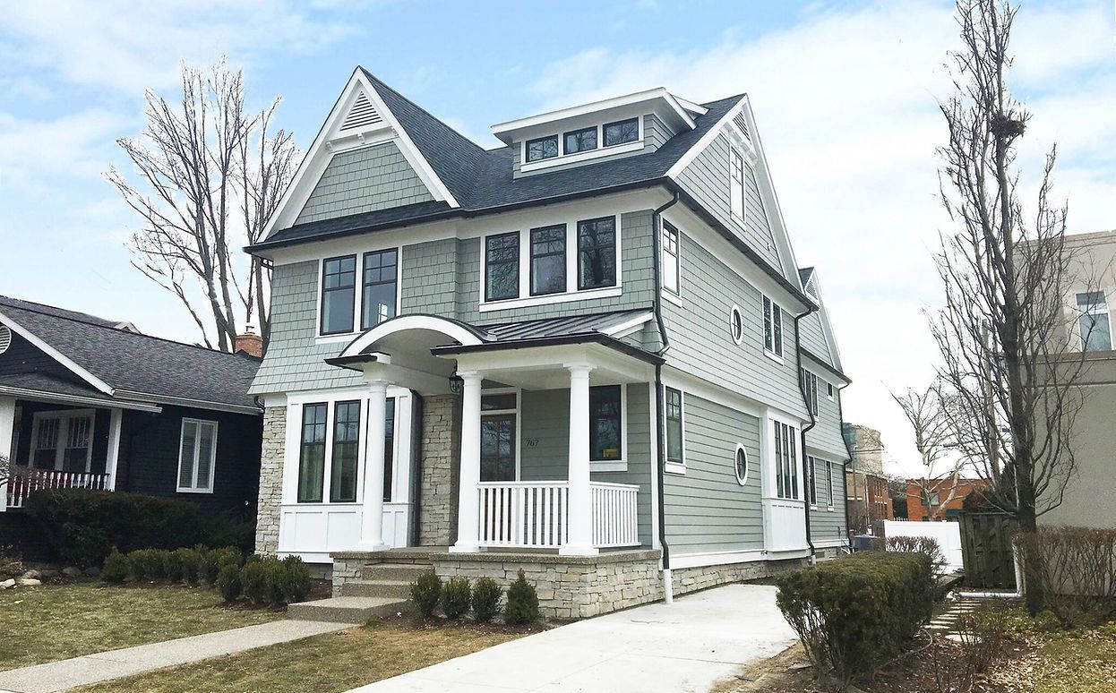 A large house with a porch and a blue roof is sitting next to a smaller house.
