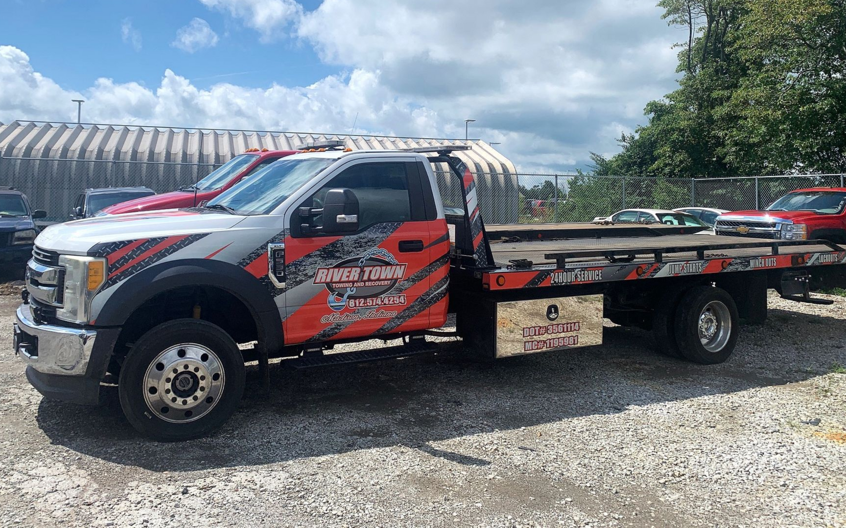 Red and silver tow truck parked on gravel under a cloudy sky.
