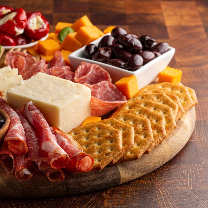 Charcuterie board with sliced meats, cheese, crackers, olives, and fruit on a wooden table