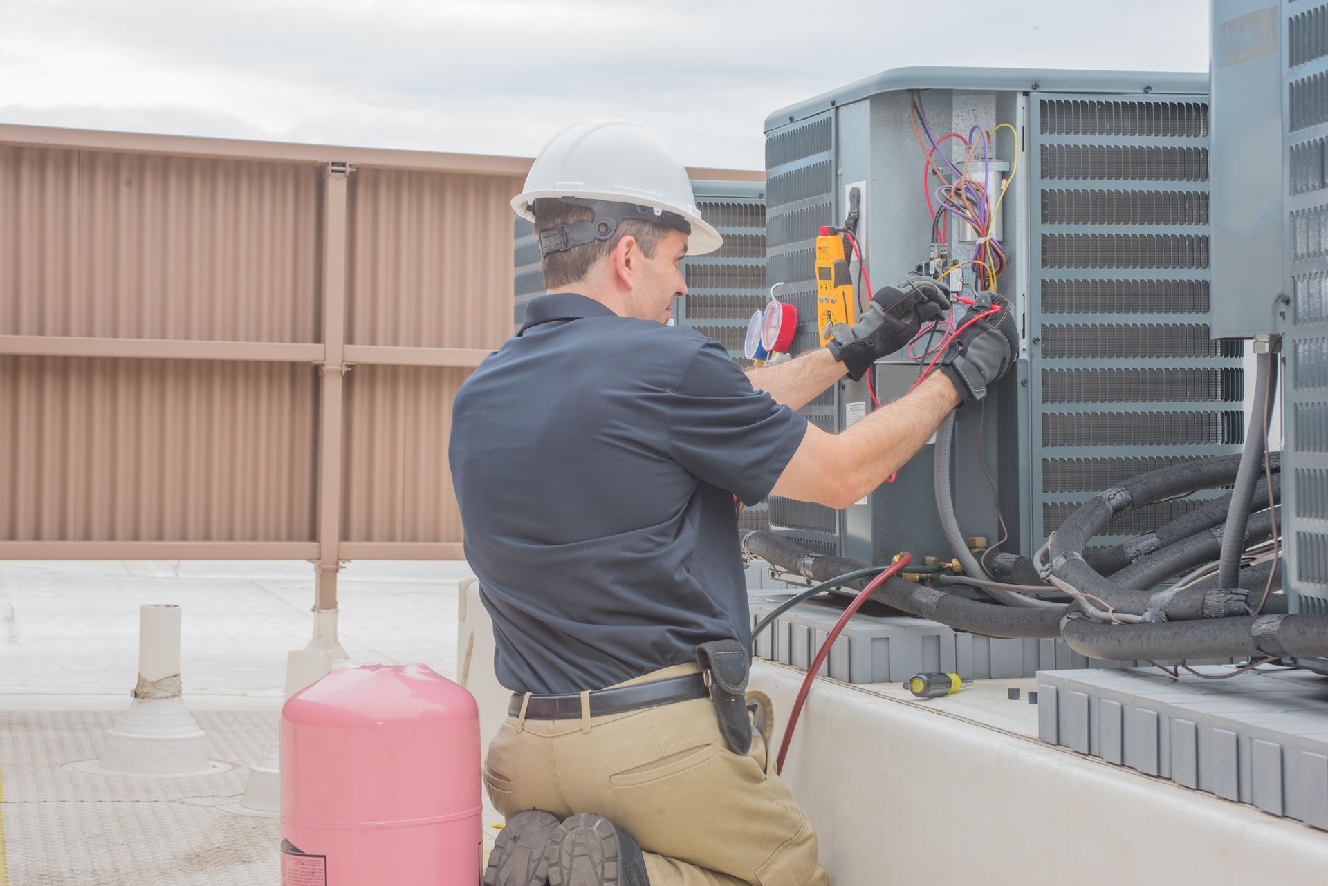 Technician in hard hat repairing rooftop HVAC unit with tools and wiring visible