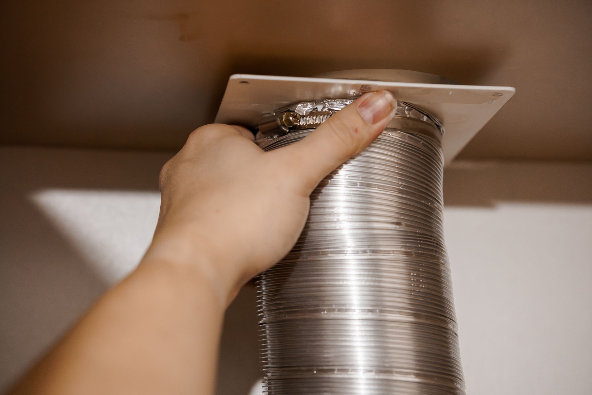Close-up of a hand connecting a duct tube to an air vent.