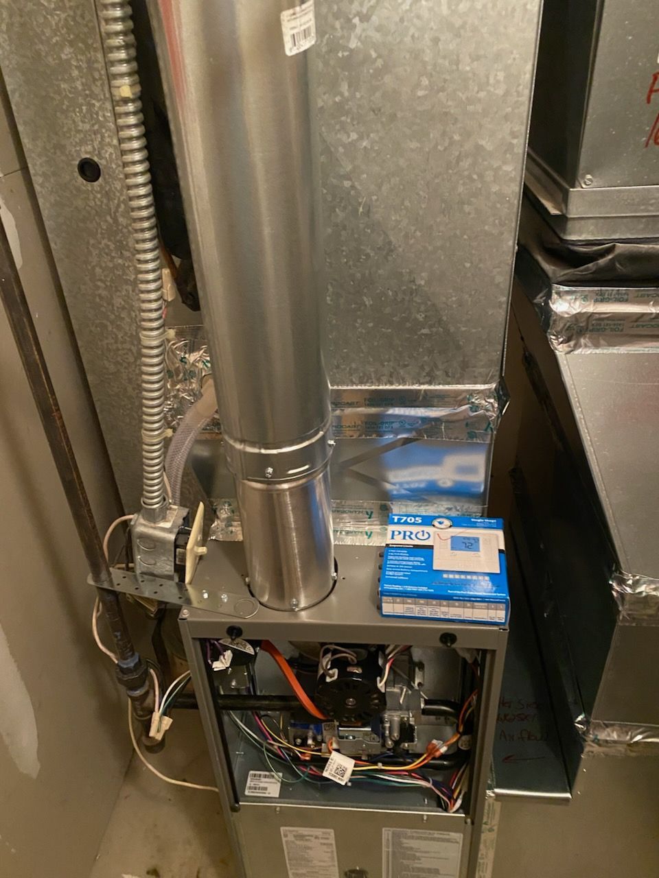 HVAC furnace with open lower panel, exposed wiring, and blue boxes resting on top.