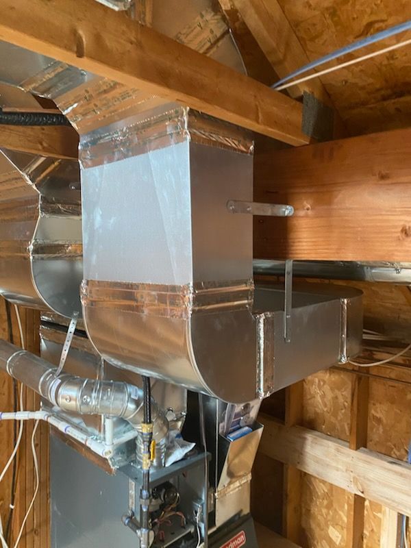 Metal HVAC ductwork in an unfinished attic with exposed wooden beams