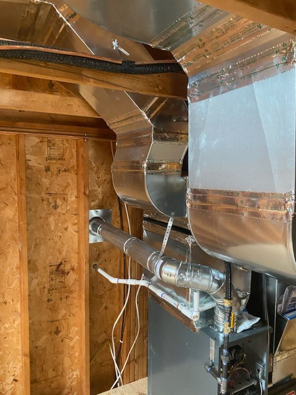 Metal HVAC ductwork and insulated pipes inside an unfinished wooden room