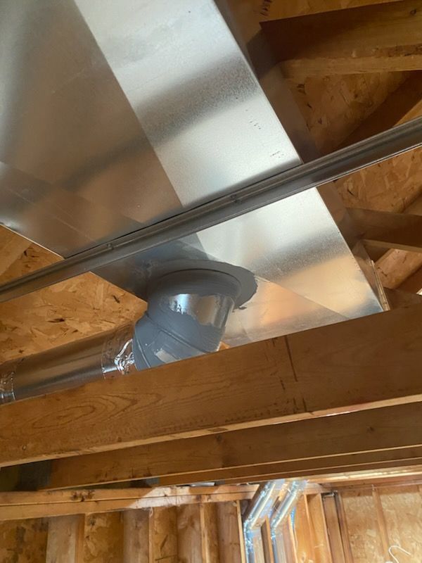 Ductwork and metal vent pipe installed in an unfinished wooden ceiling space
