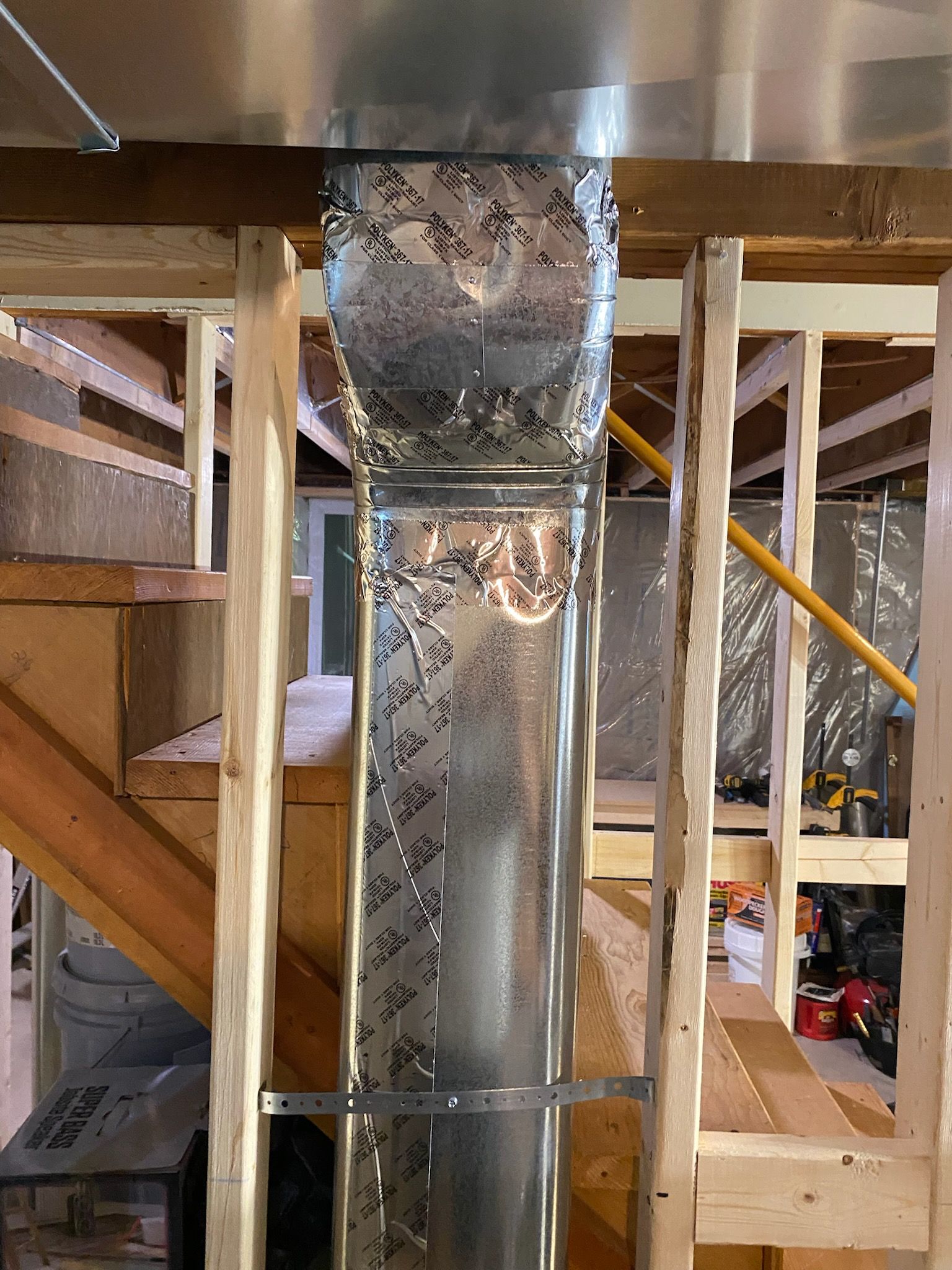 Exposed HVAC ductwork in a construction site with wooden framing and metal supports.