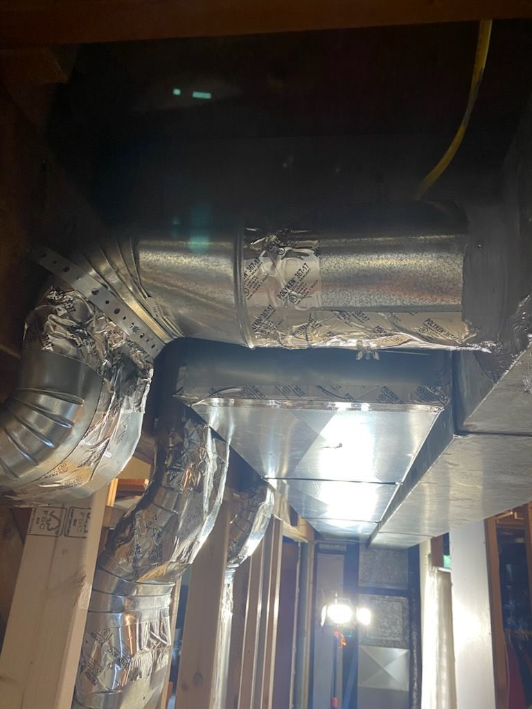 Dim industrial ceiling with shiny silver HVAC ductwork and exposed pipes under bright lights