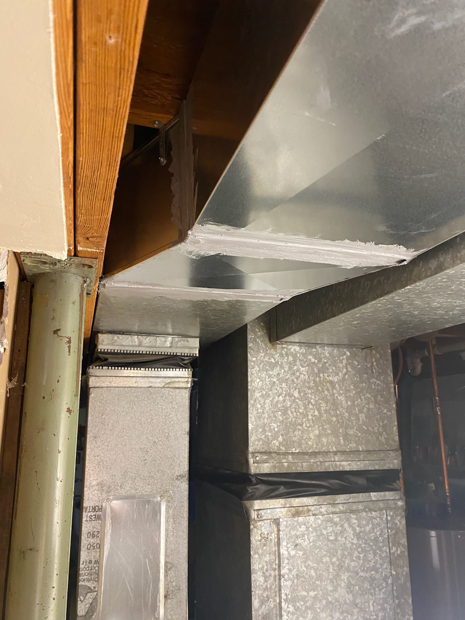 Exposed attic ductwork and insulation beside a wooden beam and metal vent pipe