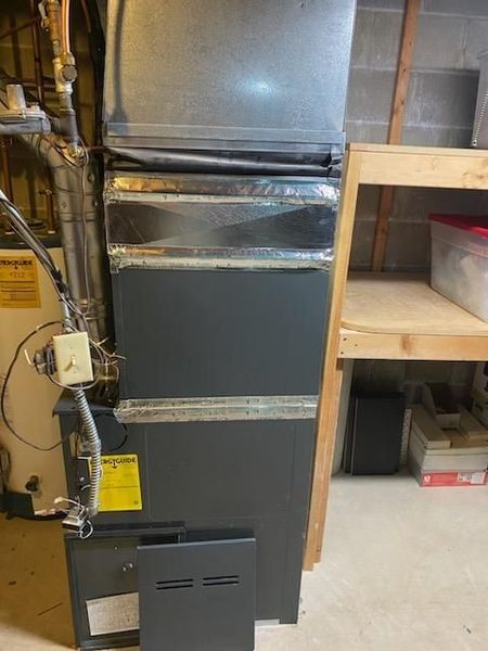 Furnace closet with ductwork, wiring, and a gray metal access panel in a utility room