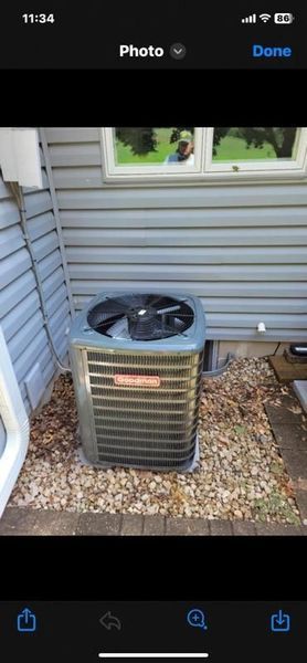 Outdoor air conditioner unit beside a house with white siding and a window, surrounded by gravel and leaves