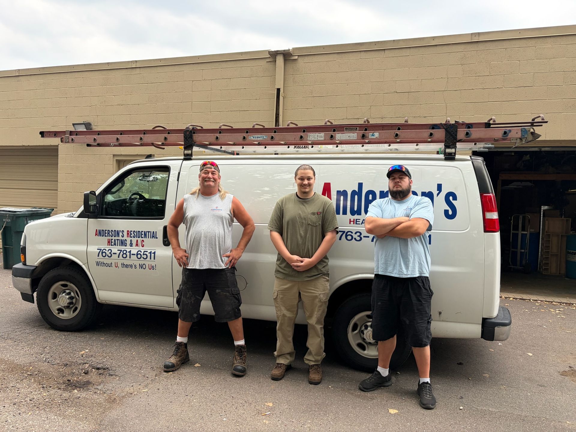 Three men standing in front of a white service van with a ladder on top.