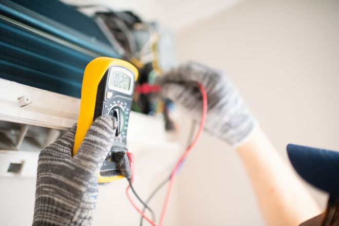 Person using a multimeter to test wiring inside an air conditioner unit