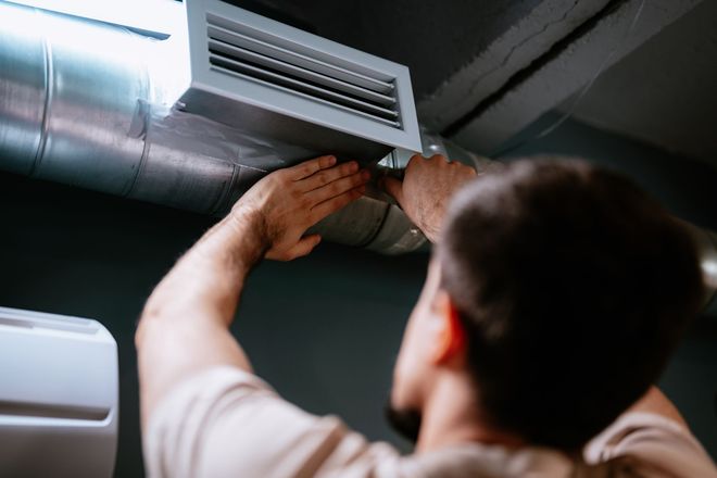 Person installing an air vent in a ceiling duct with tools