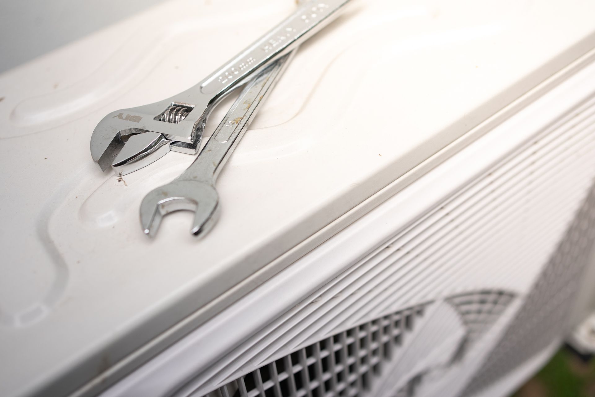 Two silver wrenches on a white air conditioner unit outdoors