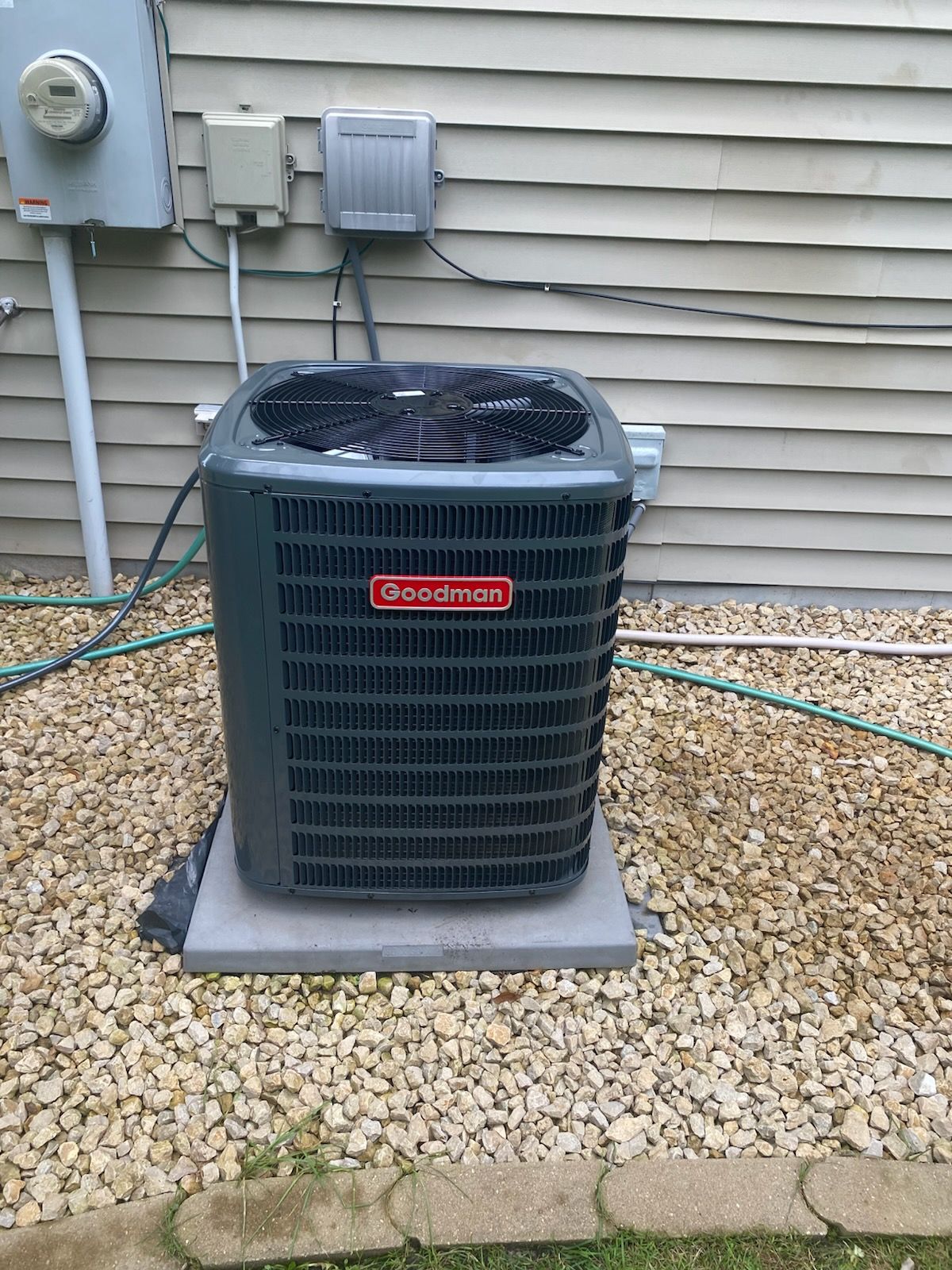 Gray air conditioner unit on gravel beside a house, with utility meters and siding in the background