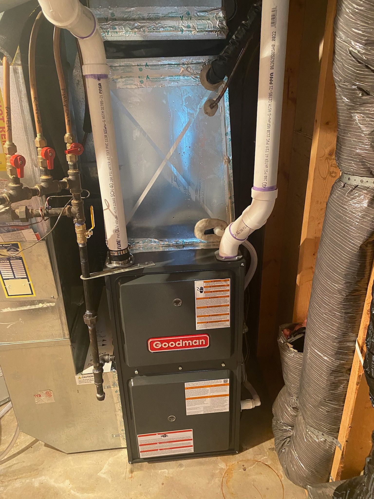 HVAC furnace unit with white pipes and insulated ducts in a basement mechanical room